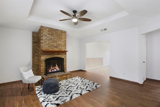 living room featuring dark hardwood / wood-style floors, a fireplace, a tray ceiling, and ceiling fan