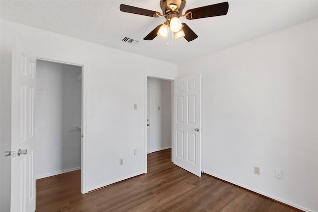 unfurnished bedroom featuring dark wood-type flooring, ceiling fan, a textured ceiling, a spacious closet, and a closet