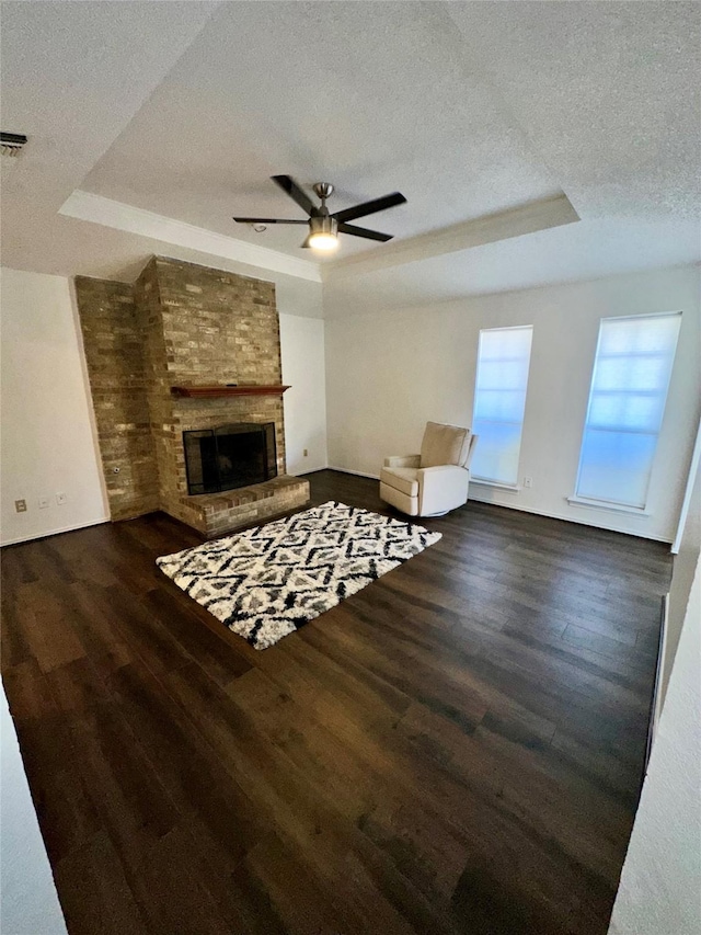 living room with dark hardwood / wood-style floors, ceiling fan, a raised ceiling, a brick fireplace, and a textured ceiling