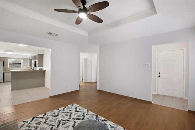 living room with a raised ceiling, ceiling fan, a textured ceiling, and light hardwood / wood-style floors