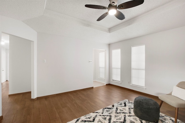 living area with a raised ceiling, ceiling fan, dark wood-type flooring, and a textured ceiling