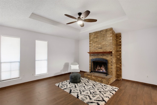 living area featuring a raised ceiling, a brick fireplace, hardwood / wood-style floors, and a textured ceiling