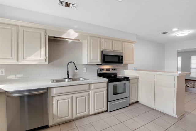 kitchen with sink, backsplash, light tile patterned floors, stainless steel appliances, and a textured ceiling