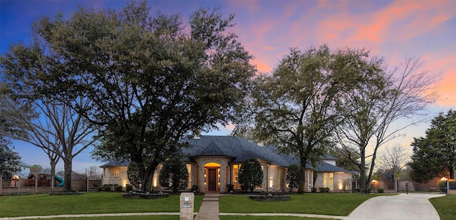 french provincial home featuring stone siding, a gate, fence, and a yard