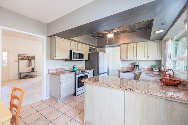 kitchen featuring sink, light tile patterned floors, appliances with stainless steel finishes, light stone counters, and a raised ceiling