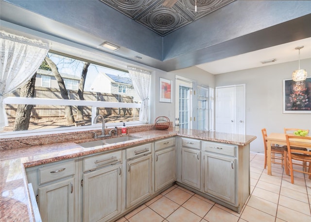 kitchen featuring sink, light tile patterned floors, hanging light fixtures, light stone counters, and kitchen peninsula