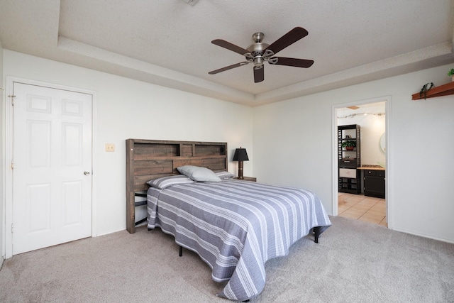 carpeted bedroom featuring a raised ceiling, connected bathroom, a textured ceiling, and ceiling fan