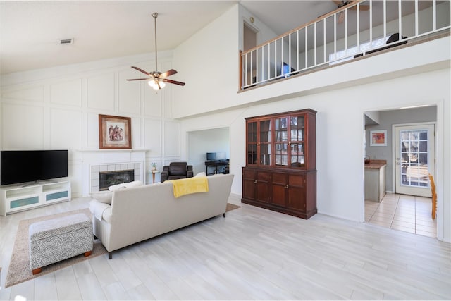 living room with ceiling fan, light hardwood / wood-style floors, high vaulted ceiling, and a tile fireplace