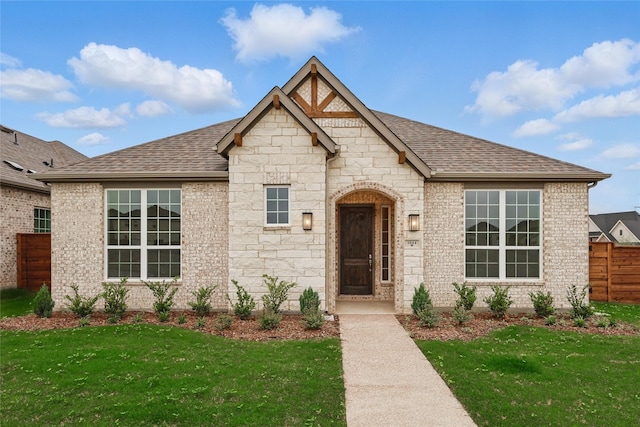 view of front of home with fence, a shingled roof, a front lawn, and brick siding