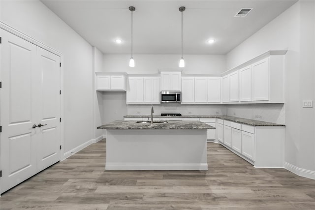 kitchen with dark stone countertops, a sink, white cabinetry, visible vents, and stainless steel microwave