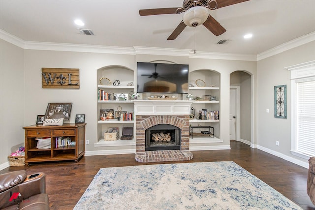 living room featuring crown molding, dark hardwood / wood-style flooring, built in shelves, and a brick fireplace