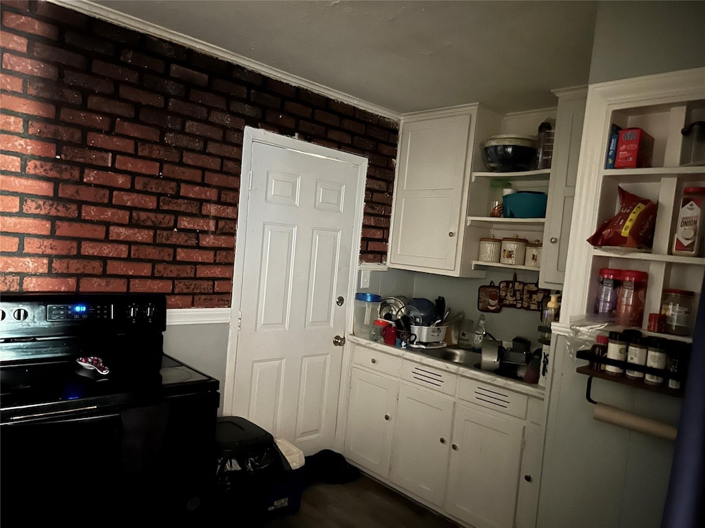 kitchen with white cabinetry, brick wall, and black range with electric cooktop