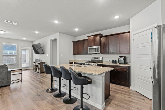 kitchen with appliances with stainless steel finishes, a kitchen island with sink, dark brown cabinetry, and light hardwood / wood-style flooring