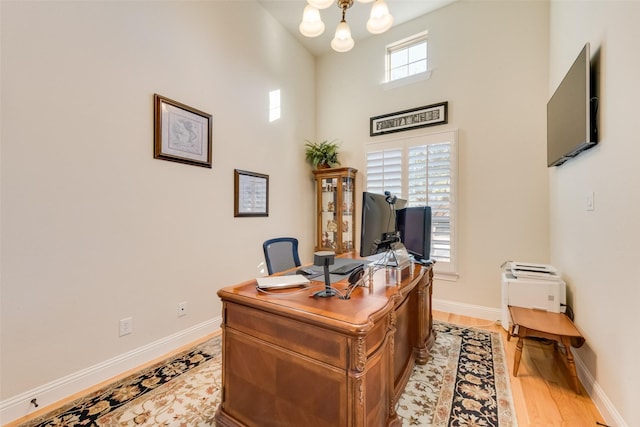 home office with a towering ceiling, a chandelier, and light wood-type flooring