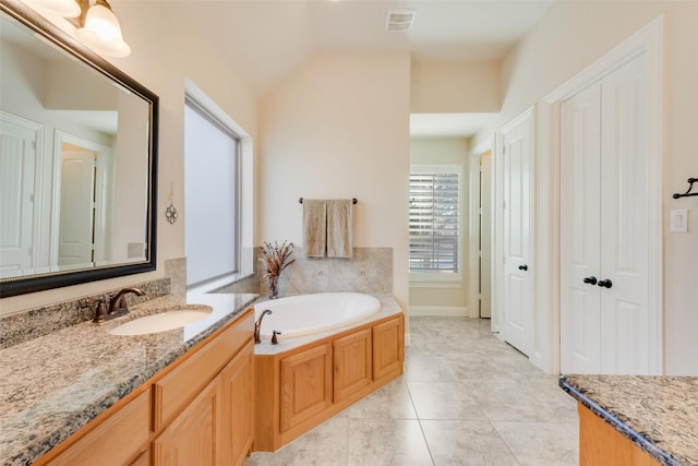 bathroom with a bathing tub, vaulted ceiling, vanity, and tile patterned floors