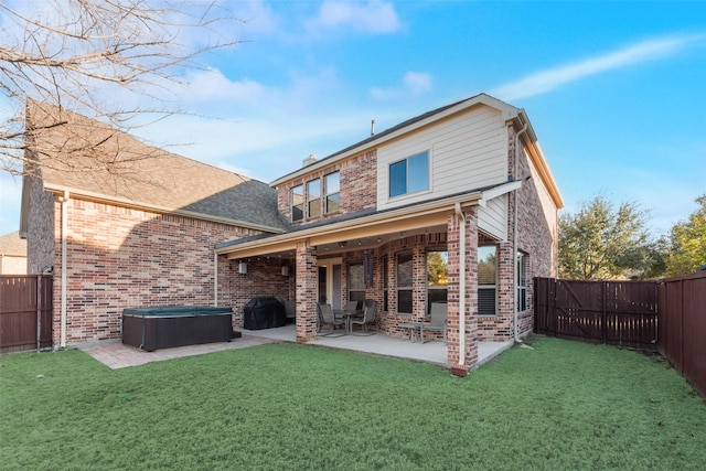 back of property featuring a hot tub, a patio, a yard, and a fireplace