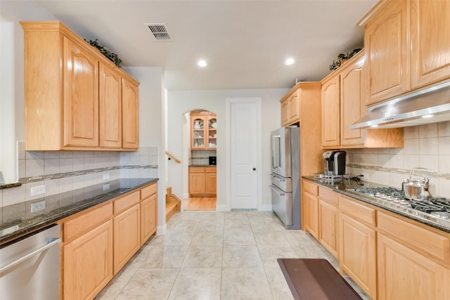 kitchen with stainless steel appliances, dark stone countertops, and light brown cabinetry