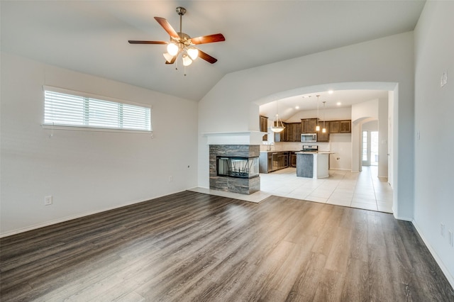 unfurnished living room featuring ceiling fan, light wood-style flooring, arched walkways, and vaulted ceiling