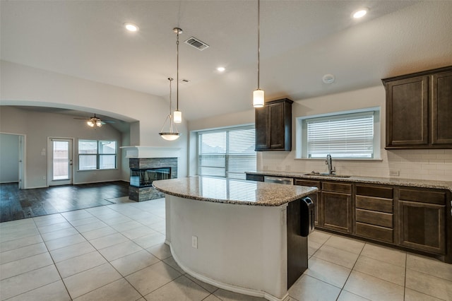 kitchen featuring arched walkways, visible vents, a sink, a stone fireplace, and dark brown cabinetry