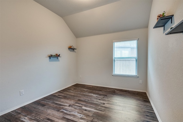 empty room featuring baseboards, vaulted ceiling, and dark wood-type flooring