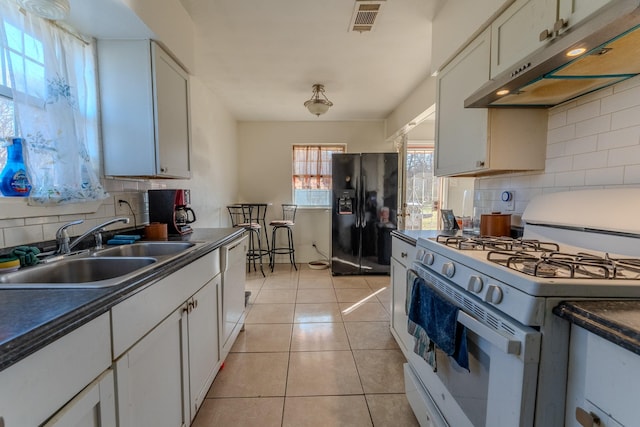 kitchen featuring sink, white appliances, light tile patterned floors, white cabinetry, and decorative backsplash