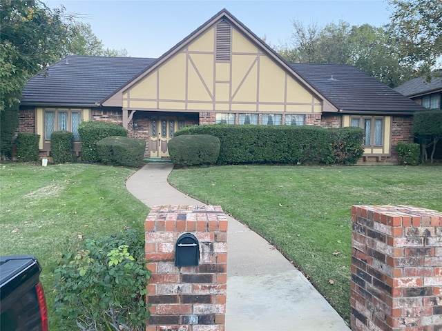 english style home with brick siding, a front lawn, and stucco siding