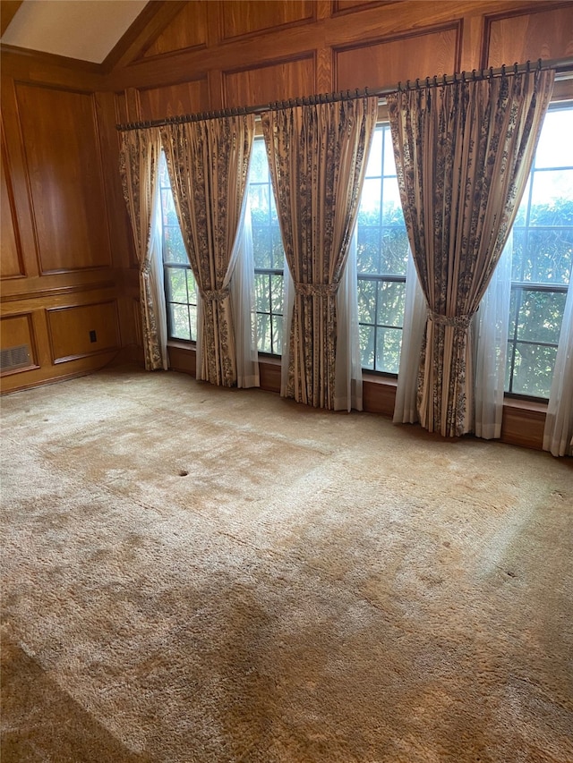 carpeted empty room featuring wood walls and visible vents