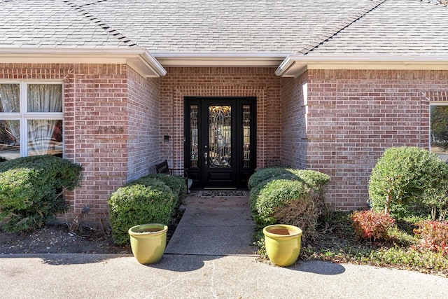 view of exterior entry featuring roof with shingles and brick siding