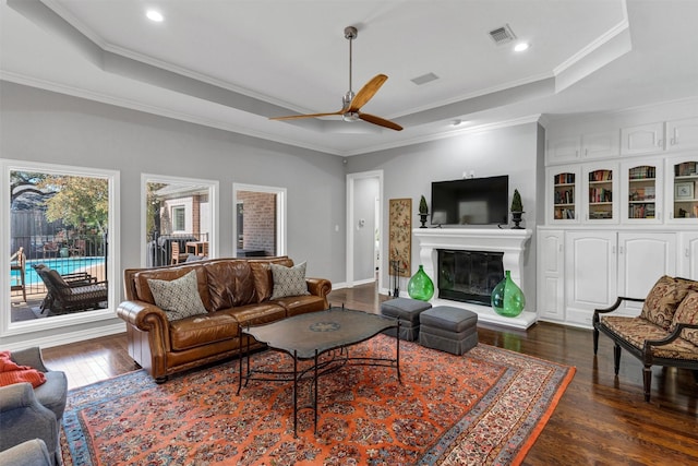 living room featuring dark wood-type flooring, ornamental molding, a raised ceiling, and ceiling fan