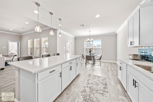 kitchen with crown molding, decorative light fixtures, a kitchen island, and white cabinets