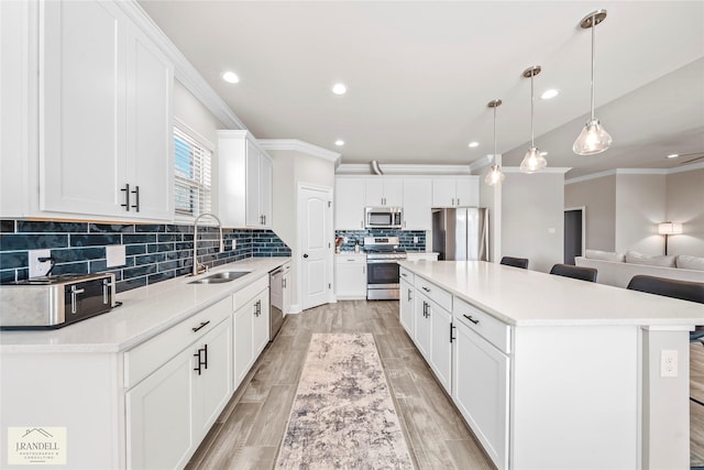 kitchen with a kitchen island, appliances with stainless steel finishes, decorative light fixtures, sink, and white cabinets