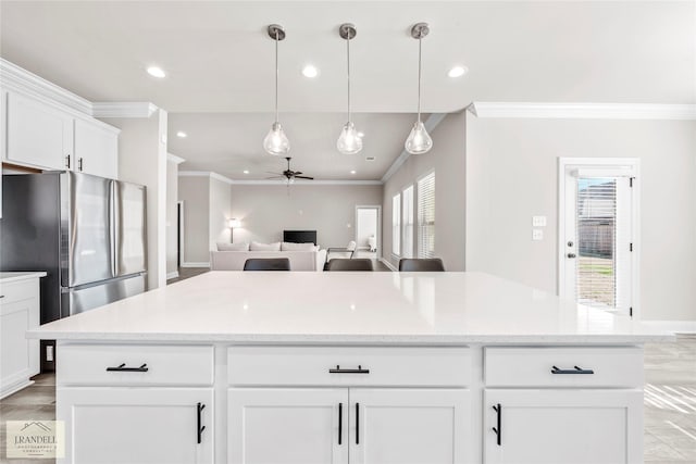 kitchen with stainless steel refrigerator, white cabinetry, hanging light fixtures, light stone counters, and ornamental molding