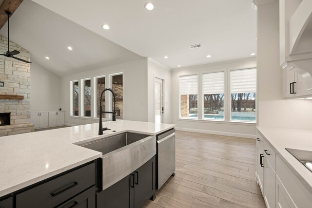 kitchen with sink, appliances with stainless steel finishes, white cabinetry, a fireplace, and a center island with sink