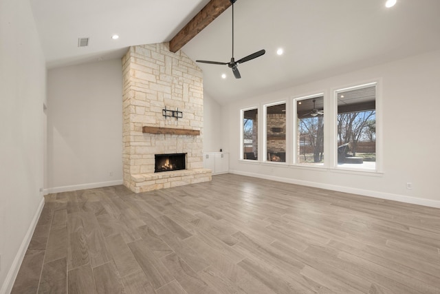 unfurnished living room with beam ceiling, a stone fireplace, a wealth of natural light, and ceiling fan