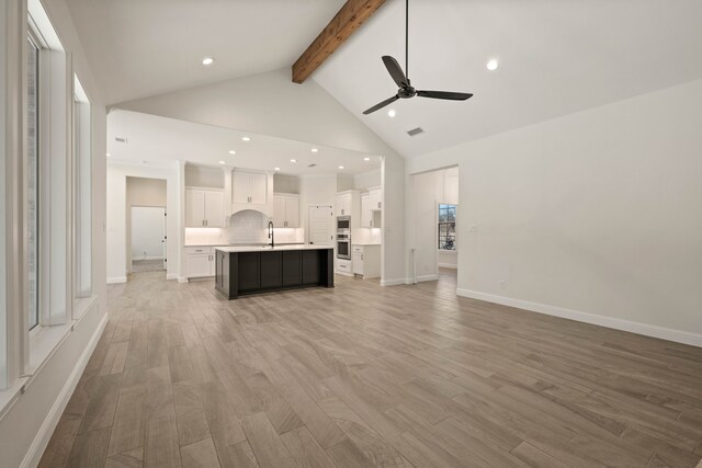 unfurnished living room featuring lofted ceiling with beams, a stone fireplace, ceiling fan, and light hardwood / wood-style flooring