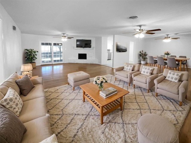 living room with ceiling fan, a brick fireplace, and light wood-type flooring