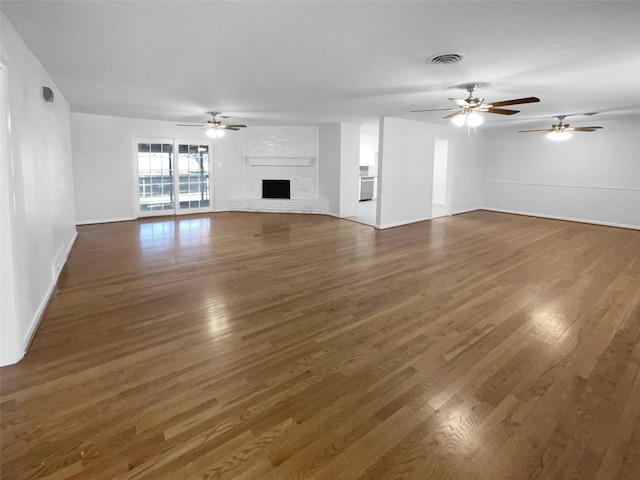 unfurnished living room featuring dark hardwood / wood-style flooring, a brick fireplace, and ceiling fan