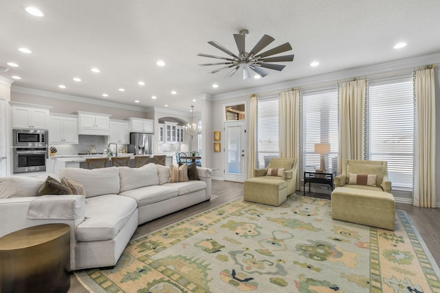 living room featuring ceiling fan with notable chandelier, ornamental molding, sink, and light wood-type flooring