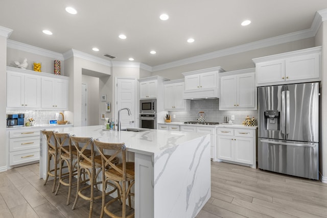 kitchen with appliances with stainless steel finishes, an island with sink, sink, white cabinets, and light stone countertops