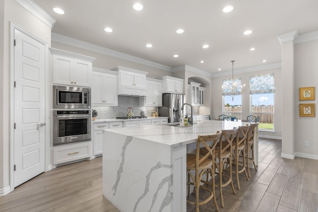 kitchen with appliances with stainless steel finishes, a kitchen breakfast bar, a spacious island, white cabinets, and decorative light fixtures