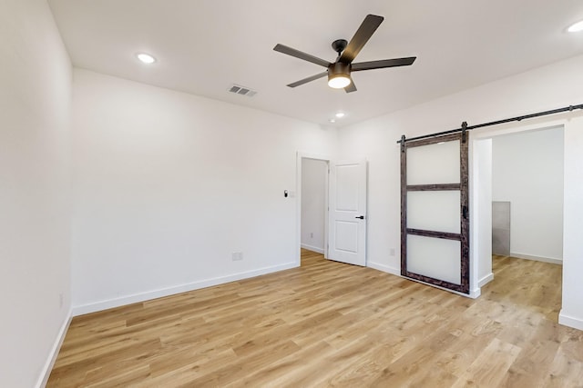 unfurnished bedroom with ceiling fan, a barn door, and light hardwood / wood-style floors