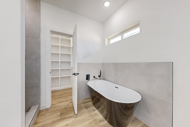 bathroom with hardwood / wood-style flooring, tile walls, and a tub to relax in