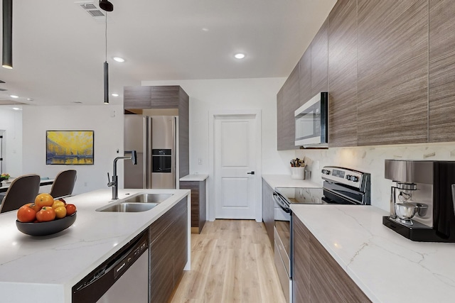 kitchen with pendant lighting, sink, stainless steel appliances, and light stone countertops