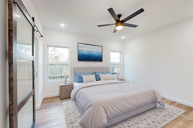 bedroom with light hardwood / wood-style floors, a barn door, and ceiling fan