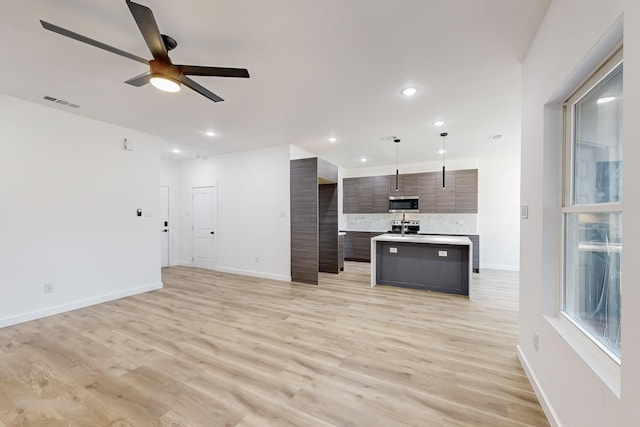 kitchen featuring dark brown cabinets, light wood-type flooring, appliances with stainless steel finishes, a kitchen island with sink, and backsplash