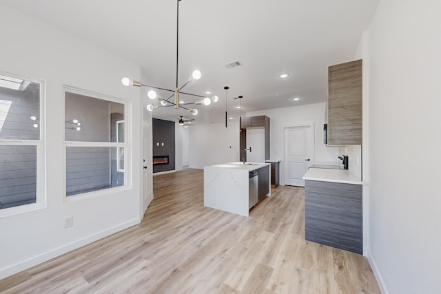 kitchen featuring sink, a kitchen island with sink, decorative light fixtures, stainless steel dishwasher, and light wood-type flooring