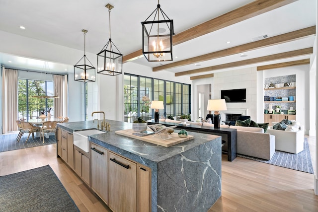 kitchen with light brown cabinetry, sink, pendant lighting, and a center island with sink