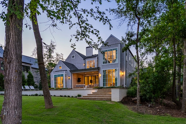 back house at dusk featuring a lawn