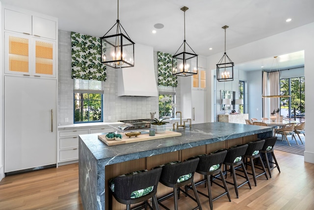 kitchen with a kitchen island, custom range hood, hanging light fixtures, and white cabinets