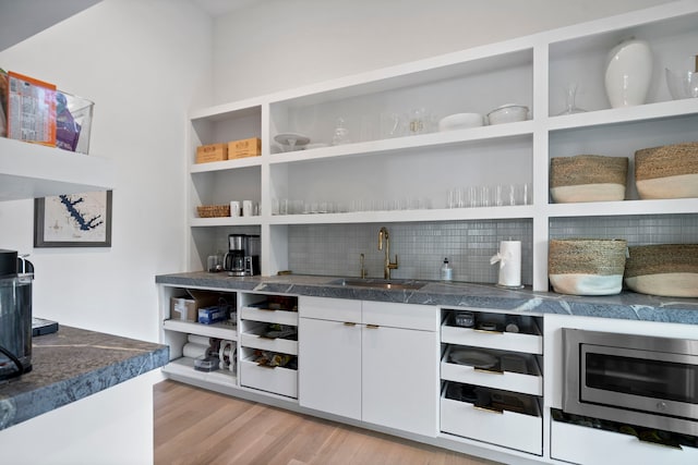 bar with sink, stainless steel microwave, light hardwood / wood-style floors, decorative backsplash, and white cabinets